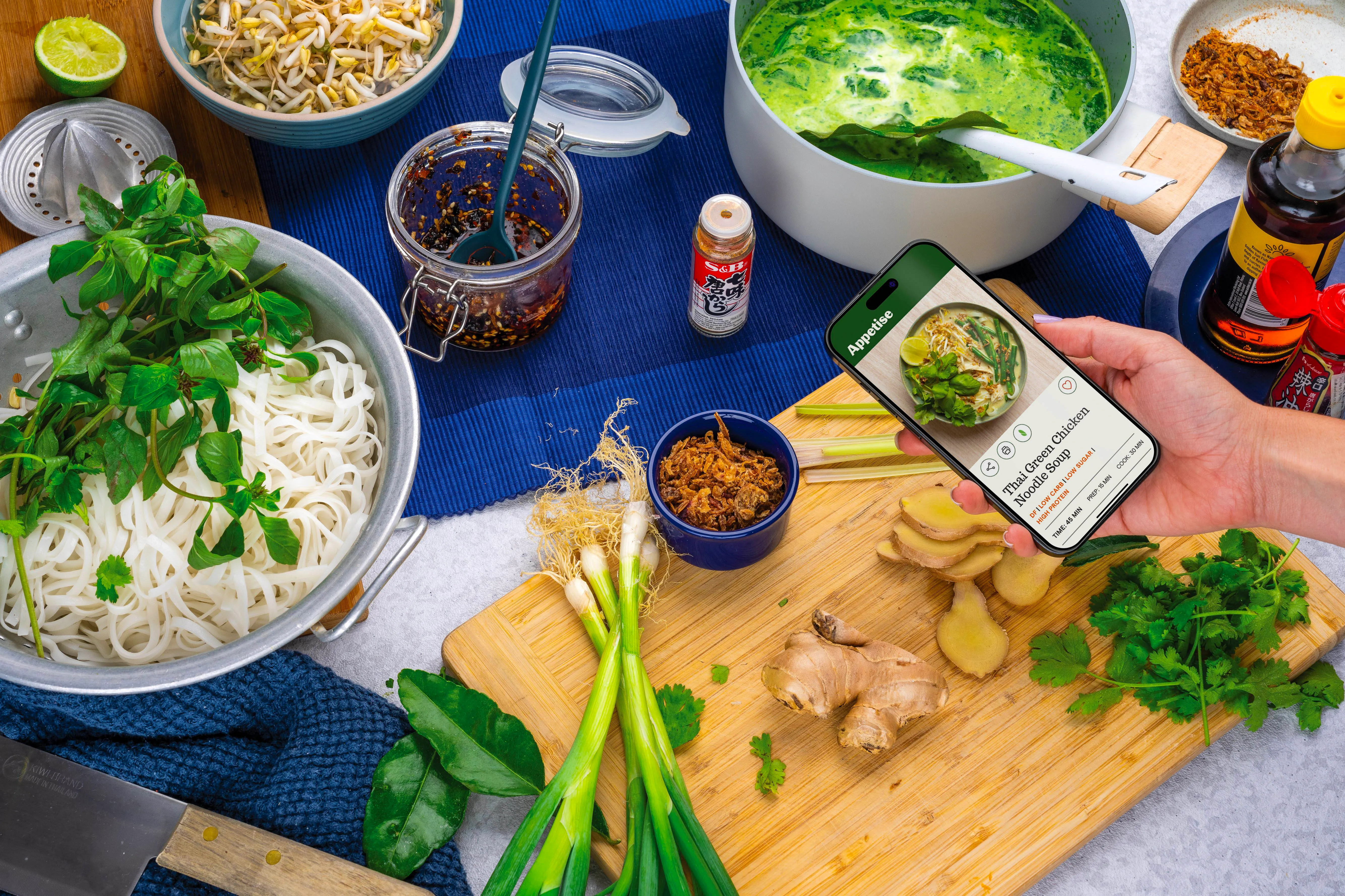A thai green curry being made on a kitchen bench, with a mobile phone showing the recipe
