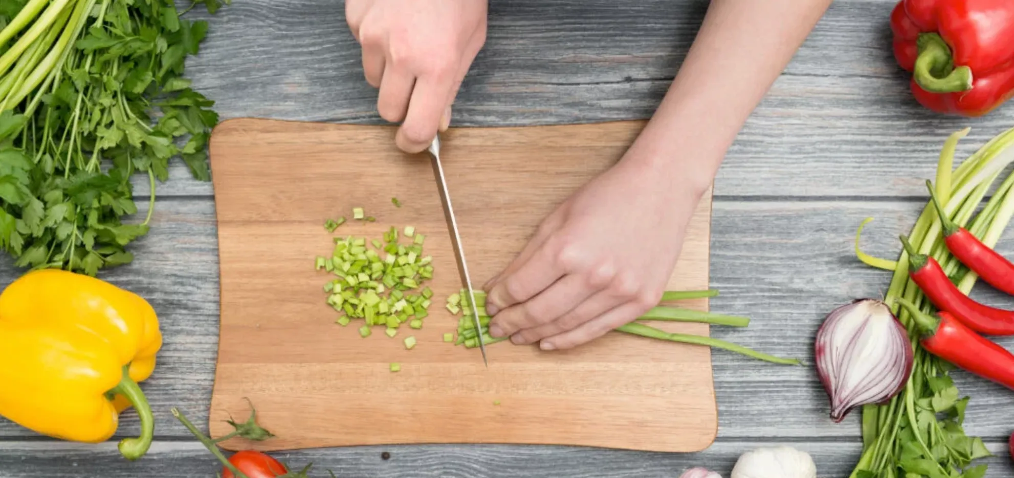 Hands chopping fresh vegetables with a knife on a shopping board