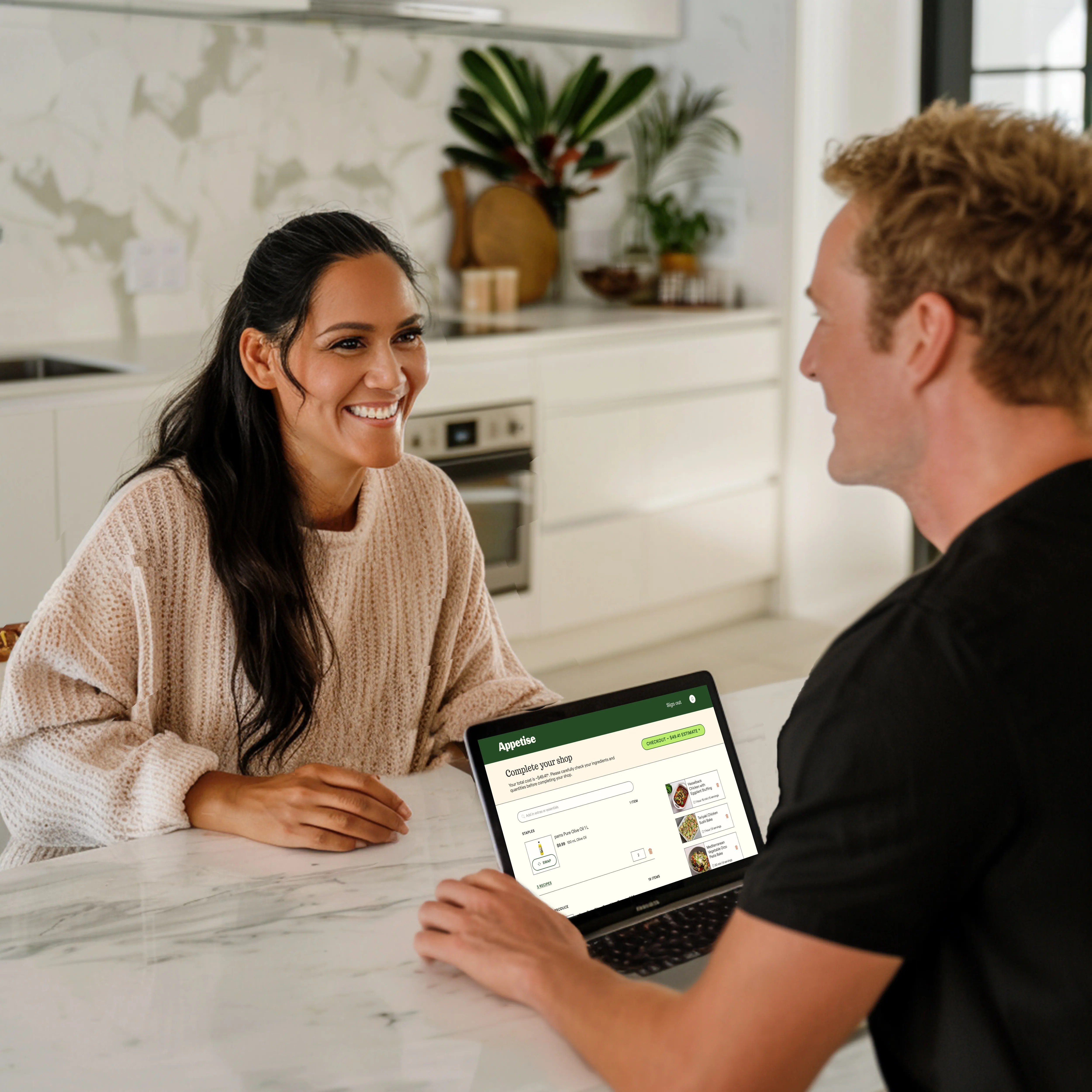 Man and women sitting in kitchen using laptop